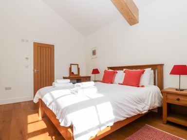 A bedroom with a wooden bed and red cushions two bedside tables and lamps a wooden door and a small desk with a mirror at Wheal Grey in Praa Sands