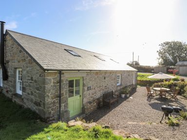 A stone cottage with a green door a bench and an outdoor seating area with a table umbrella and barbecue at Wheal Grey in Praa Sands