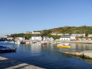 A harbor with boats on water and houses on a hillside at Wheal Grey in Praa Sands