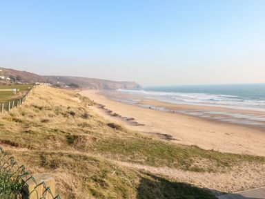 A sandy beach with waves and grassy dunes along the shore at Wheal Grey in Praa Sands