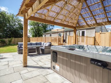 A patio with a hot tub and outdoor seating under a wooden pergola at Kelyow in St Day