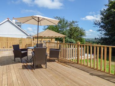 A wooden deck with a round table and four chairs under a large umbrella at Kelyow in St Day