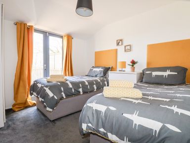 A bedroom with two single beds, grey bedding with white animal prints, orange headboards and curtains at Kelyow in St Day