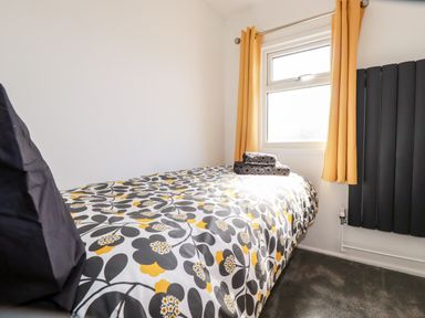 A bedroom with a single bed with a floral bedspread next to a window with yellow curtains and a black radiator at Kelyow in St Day