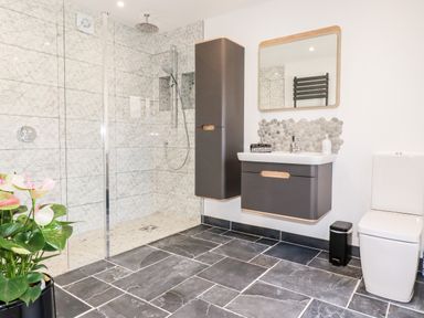 A bathroom with a walk in shower toilet sink mirror and wall cabinets at Kelyow in St Day