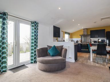 A living area with a round chair next to glass doors and a kitchen with dining table and chairs at Kelyow in St Day