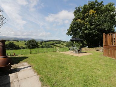 A garden with a metal table and chairs with an umbrella and a view of green fields and hills at Hen Stabl in Llanrwst