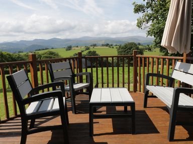 An outdoor deck with four chairs a table and a large umbrella overlooking green fields and hills at Hen Stabl in Llanrwst