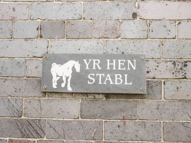 A wall sign with a horse illustration and the text YR HEN STABL on a brick wall at Hen Stabl in Llanrwst