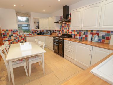 A kitchen with a white dining table and chairs and colorful tiled backsplash at Hen Stabl in Llanrwst