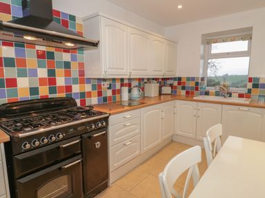 A kitchen with white cabinets colorful tile backsplash black stove table and chairs next to a window at Hen Stabl in Llanrwst