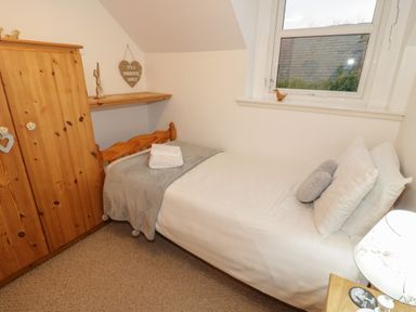 A small bedroom with a single bed wooden wardrobe and a window at Hen Stabl in Llanrwst