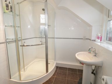 A bathroom with a corner shower enclosure a pedestal sink and a window with toiletries at Hen Stabl in Llanrwst