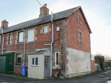 A brick end terrace house with a grey door and small window extension at Corbett Cottage in New Haggerston near Holy Island