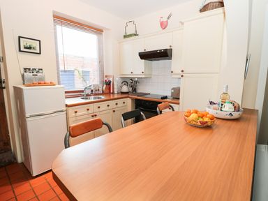 A kitchen with wooden countertops white cabinets a refrigerator a stove and a wooden table with bowls of fruit at Corbett Cottage in New Haggerston near Holy Island