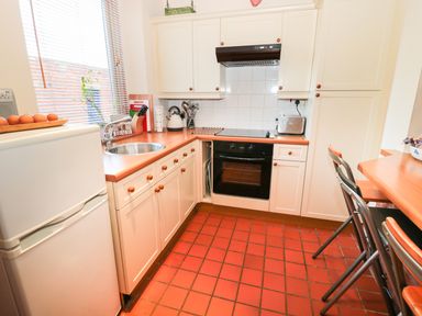 A kitchen with white cabinets a black oven a stainless steel sink a refrigerator and two stools at Corbett Cottage in New Haggerston near Holy Island
