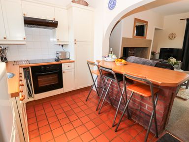A kitchen with a wooden countertop bar and stools next to a living room with a television at Corbett Cottage in New Haggerston near Holy Island