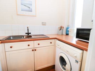 A kitchen with a sink microwave washing machine utensils and a framed picture on the wall at Corbett Cottage in New Haggerston near Holy Island
