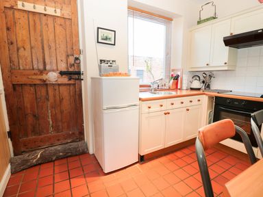 A kitchen with wooden door white refrigerator sink and oven at Corbett Cottage in New Haggerston near Holy Island