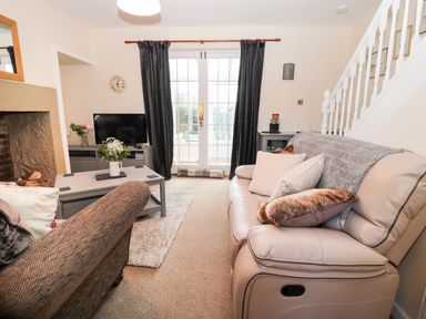 A living room with sofas a coffee table flowers a television and stairs at Corbett Cottage in New Haggerston near Holy Island