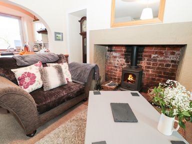 A living room with a fireplace a sofa and a coffee table with flowers at Corbett Cottage in New Haggerston near Holy Island