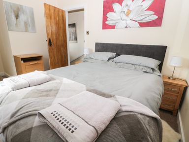 A bedroom with a double bed with gray bedding and towels on it bedside tables with lamps wooden door and paintings on the walls at Corbett Cottage in New Haggerston near Holy Island