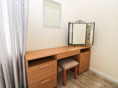A wooden dressing table with drawers and a stool with a three-panel mirror on top and a curtain on the left at Corbett Cottage in New Haggerston near Holy Island
