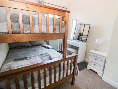 A bedroom with a wooden bunk bed a white dressing table with a mirror a white nightstand and a lamp at Corbett Cottage in New Haggerston near Holy Island