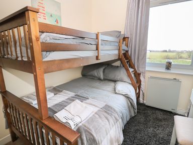 A bedroom with wooden bunk bed gray bedding a window with a view and a small heater on a dark carpet at Corbett Cottage in New Haggerston near Holy Island