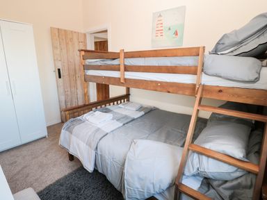 A bedroom with a wooden bunk bed a white wardrobe a wooden door and a painting of a lighthouse at Corbett Cottage in New Haggerston near Holy Island
