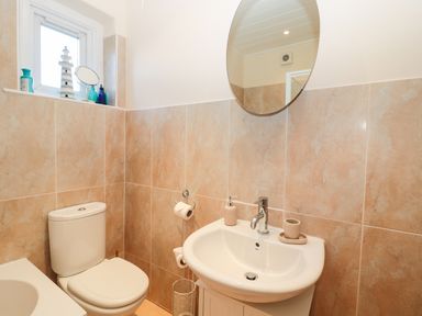 A bathroom with a toilet a sink a round mirror and a window with decorative items at Corbett Cottage in New Haggerston near Holy Island
