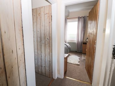 A hallway with wooden doors leading to a bedroom with curtains and a small rug at Corbett Cottage in New Haggerston near Holy Island