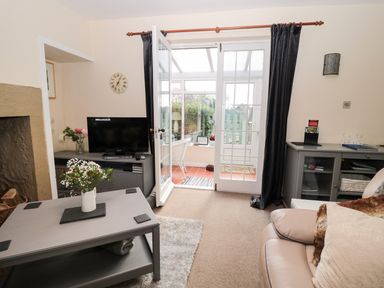 A living room with a coffee table a television and a glass door leading to a sunroom at Corbett Cottage in New Haggerston near Holy Island