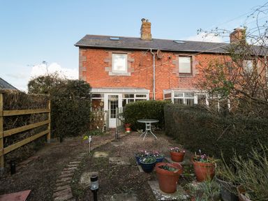 A backyard garden with potted plants and a table behind a brick house at Corbett Cottage in New Haggerston near Holy Island