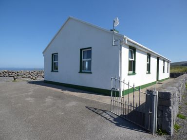 A single-story white house with green trim around windows and base with a paved driveway and metal gate at Seaview Cottage in Fanore County Clare