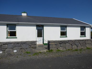 A white single-story house with three windows a door and a stone wall in front at Seaview Cottage in Fanore County Clare