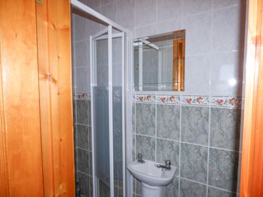 A bathroom with a shower enclosure pedestal sink wall mirror and tiled walls at Seaview Cottage in Fanore County Clare