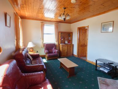 A living room with red leather sofas a wooden coffee table a wooden cabinet and a TV stand at Seaview Cottage in Fanore County Clare