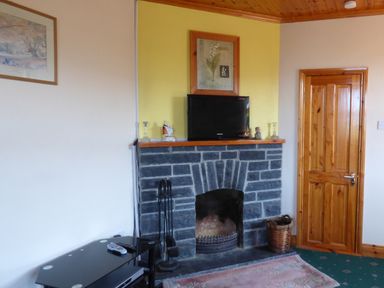 A room with a stone fireplace a television on the mantel a wooden door and a black table with remotes at Seaview Cottage Fanore County Clare