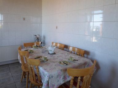 A dining room with a table covered in floral tablecloth six wooden chairs cups plates and a teapot at Seaview Cottage in Fanore County Clare