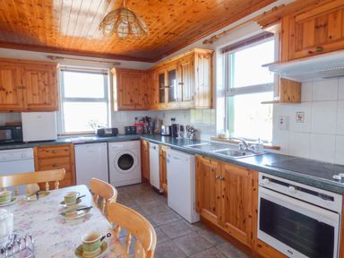 A kitchen with wooden cabinets appliances and a dining table with cups at Seaview Cottage in Fanore County Clare