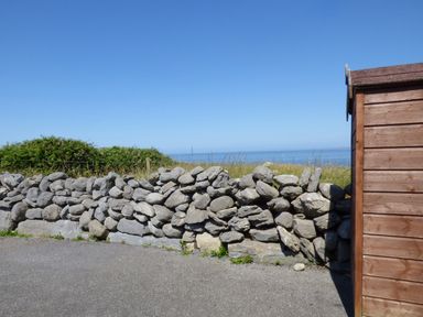 A stone wall next to a gravel path with grass bushes and the sea in the background at Seaview Cottage in Fanore County Clare