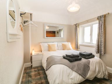A bedroom with a bed with pillows and towels beside a window and a mirror at The Beach House Criccieth in Criccieth