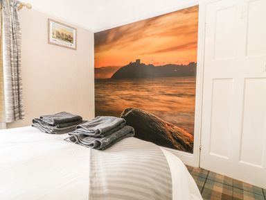 A bedroom with a bed with folded towels and a large wall mural of a sunset over water at The Beach House Criccieth