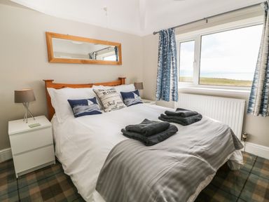 A bedroom with a bed with pillows and folded towels a window with curtains two bedside tables with lamps and a mirror on the wall at The Beach House Criccieth