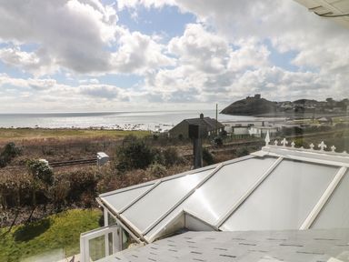 A coastal view with a garden and railway tracks overlooking the sea and a hill with a castle at The Beach House Criccieth