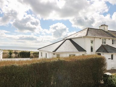 A white house with a hedge in front and the sea in the background at The Beach House Criccieth