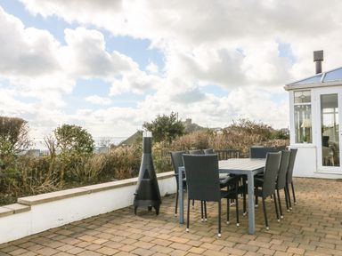 An outdoor patio with a dining table and chairs next to a white building and plants at The Beach House Criccieth