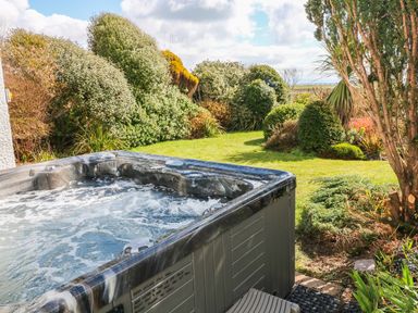 A bubbling hot tub next to a garden with grass and various bushes at The Beach House Criccieth