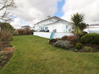 A garden with green grass shrubs and a white house with a terrace and a slide at The Beach House Criccieth